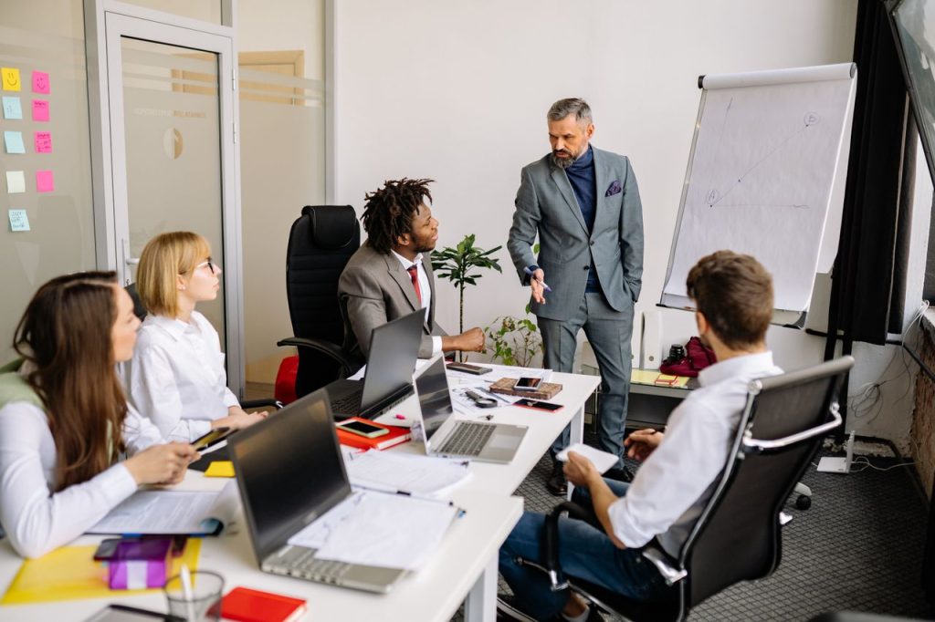La vida no exige perfección, exige constancia Corporate team in a modern office, engaged in a discussion with diverse colleagues.